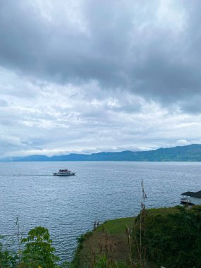 Bir feribot uzak dağlarla bulutlu bir gökyüzünün altında büyük bir su kütlesi boyunca seyahat eder..