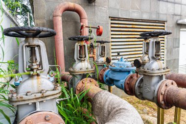 Paslı kırmızı boruları, vanaları, göstergeleri ve beyaz bir duvara karşı belirgin bir alarmı olan bir açık hava fıskiye sistemi..