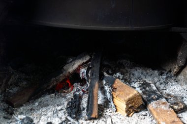 Close-up of burning firewood with bright red embers and ash in a dark fireplace. clipart