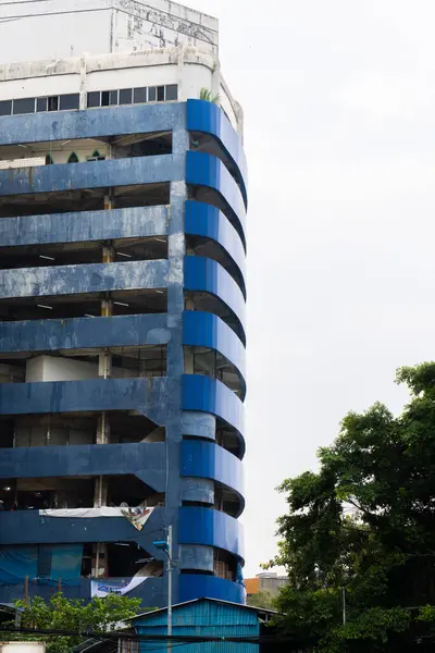 Uzun, çok katlı bir otopark mavi aksanlı, yapraklı yeşil ağaçlara bitişik..