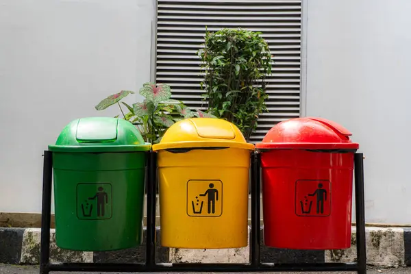 Üç renkli çöp tenekesi, yeşil, sarı ve kırmızı, beyaz bir duvarın önünde dururlar..