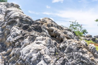 Karmaşık desenli yıpranmış bir kaya oluşumu açık bir gökyüzünün altında, açık hava manzarası temalarına uygun doku ve doğal oluşumları gösterir..