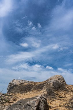 Kayalık bir çıkıntı dinamik mavi bir gökyüzünün altında duruyor. İnce bulutlar sürükleniyor ve manzaralı bir manzara yaratıyor..