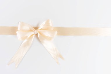 Yumuşak, kremsi sarı bir kurdele zarif bir şekilde parlak beyaz arka planda bir yayla bağlanır..