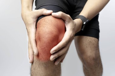Bir adam acı içinde dizini tutar, kırmızı bölge iltihaplanma ve rahatsızlık göstergesidir. Spor giysisi giyiyor..