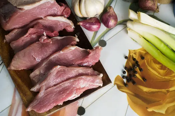 Tahtada ince dilimlenmiş çiğ domuz eti, sarımsak, arpacık soğanı, soğan ve biberli. Lezzetli bir yemek hazırlığı için hazır..