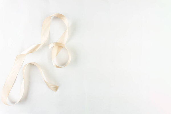 Атласная лента из слоновой кости, элегантно скрученная на ярком белом фоне, излучает изысканность и минималистский шарм.
