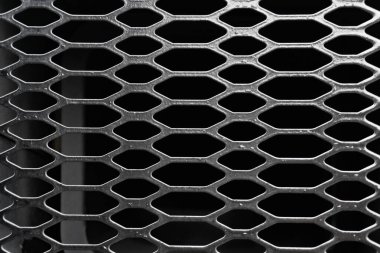 A close-up of a metal mesh or grill, featuring a repeating pattern of oval or diamond-shaped openings.