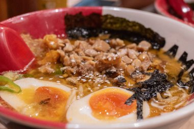 İçinde erişte, çorba, yarı pişmiş yumurta, yosun ve doğranmış et bulunan bir kase ramen..