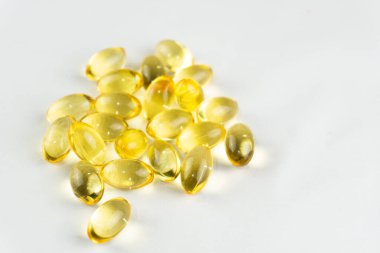 A pile of golden-colored Omega 3 softgels on a white background, promoting health and nutrition.