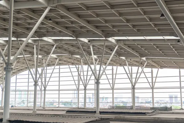 The structure of a station, featuring steel beams, girders, and metal structures. In the background, a city skyline is visible.