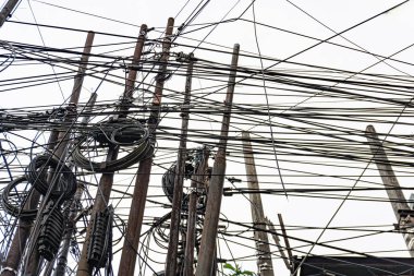 Parlak bir gökyüzüne karşı elektrik kablolarından ve direklerden oluşan karışık bir ağ, şehir altyapısında kaos yaratıyor..