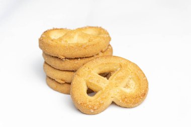 Tereyağlı kurabiyelerden oluşan altın bir deste, beyaz bir zemin üzerine kurulmuş, bu tatlı ikramların dokusunu ve cazibesini vurguluyor..