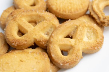 Çeşitli tereyağlı kurabiyelerden oluşan yakın çekim beyaz arka planda eşsiz şekillerini, altın renklerini ve şekerli yüzeylerini vurgular..