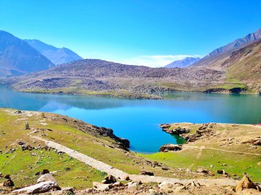 Mavi renkli güzel göl, arka planda dağlar ve ön planda kayalar. 