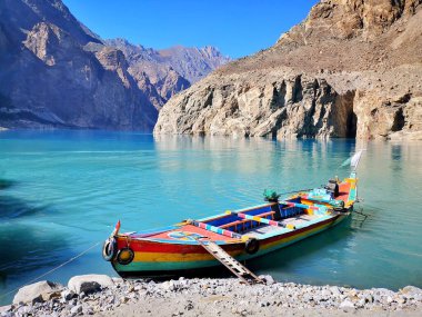 Gölde renkli bir tekne, arkasında dağlar var.