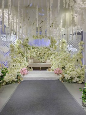 Ortasında beyaz kanepe ve perde arkasında pembe ve beyaz çiçekler olan bir düğün için şık dekore edilmiş bir sahne. 