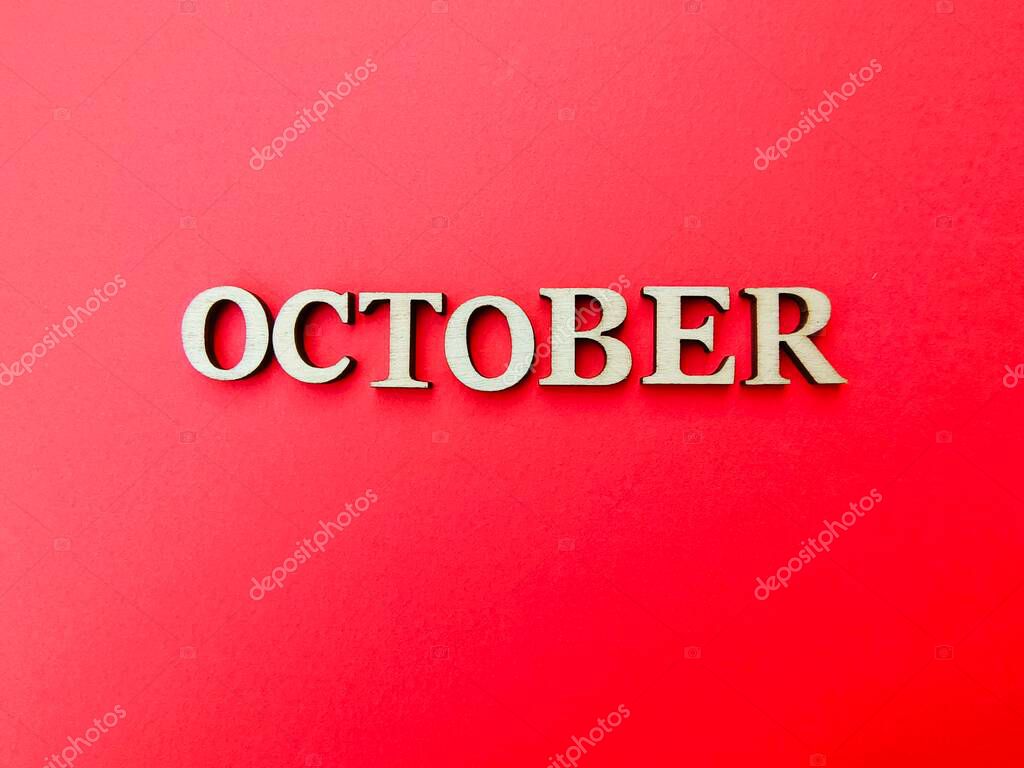 A bright, minimalist composition featuring wooden letters spelling October, symbolizing breast cancer awareness, support, and hope in a clean, modern layout. Flat lay text on red background