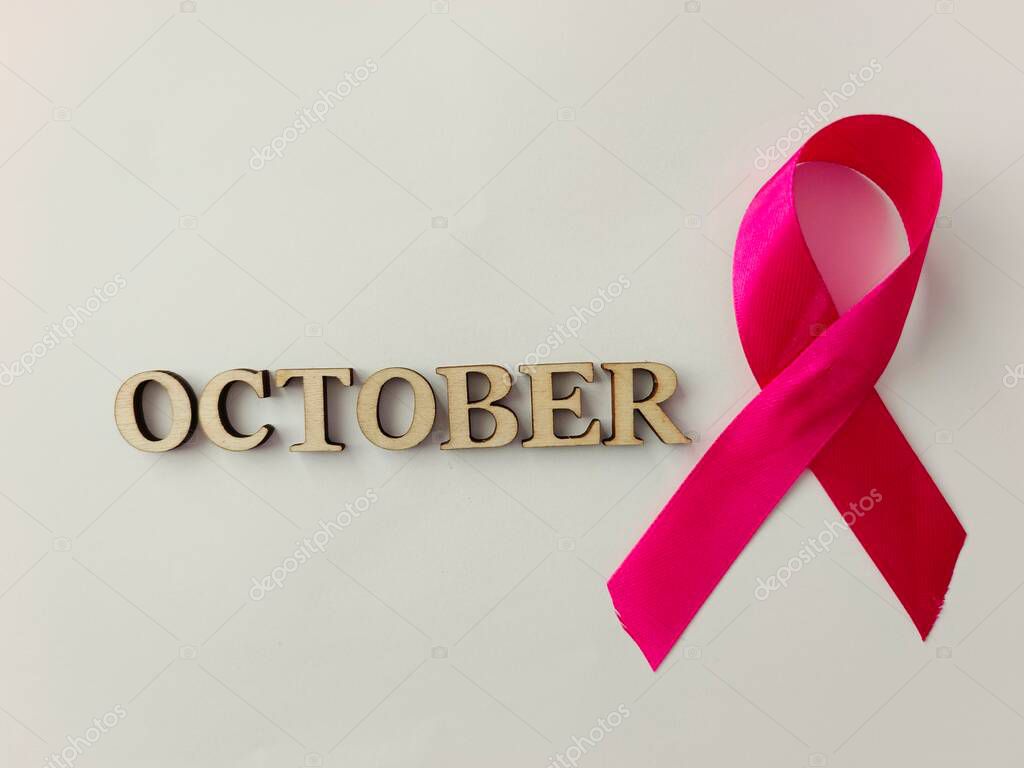 A bright, minimalist composition featuring a vivid pink ribbon beside wooden letters spelling Pink October, symbolizing breast cancer awareness, support and hope in a clean, modern layout