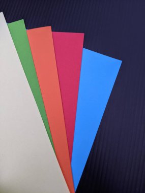 Çeşitli renkli kağıt çarşaflar derin bir kömür arka planına karşı bir yelpazede düzenlenmiştir, görsel ilham için yaratıcı projeler, el sanatları, kolaj ve canlı tasarım fikirleri önerilir