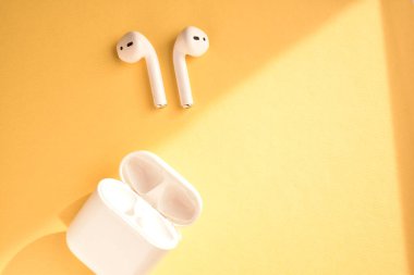 Sarı arka planda beyaz kablosuz kulaklık.