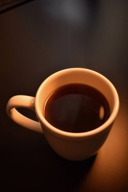 Masanın üzerinde sade, sıcak kahve olan beyaz bir fincan.