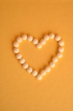 Sarı arka planda kalp şeklinde düzenlenmiş hap ve hap paketleri.