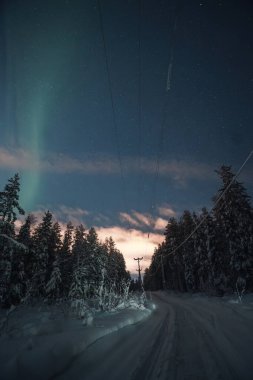 Rovaniemi, Laponya 'daki kar motorlu rayların ve elektrik hatlarının üzerinde sönük bir aurora.