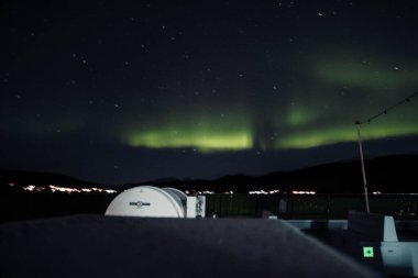 Tromso, Norveç 'teki yolcu gemisinin üstündeki yıldızlı gökyüzünde güçlü Aurora Borealis.