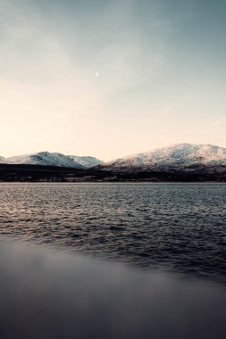 Norveç, Tromso 'nun dışındaki fiyordun yanındaki karlı arktik dağ silueti.