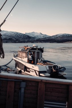 Norveç 'in Tromso kentindeki dağların yakınındaki Kuzey Kutbu fiyortlarında balıkçı teknesinde bir adam var.