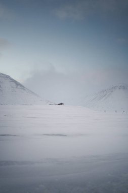 Longyear, Svalbard yakınlarında, gün batımında gökyüzünün altında karlı kutup vadisindeki kulübe.
