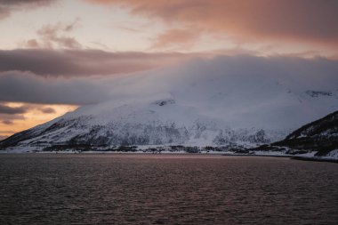 Kuzey Norveç 'te, bulutların altındaki karlı arktik dağlar altın saat.