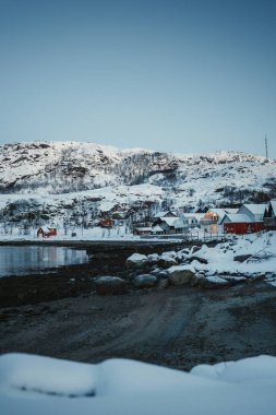 Norveç, Tromso yakınlarındaki Ersfjordbotn 'da karlı evlerin yanındaki Rocky Arctic plajı..