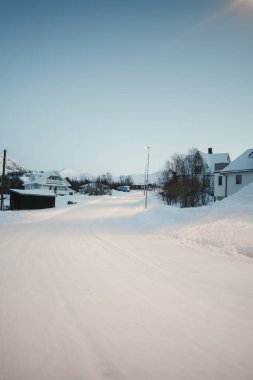 Norveç, Tromso yakınlarında, güneş doğarken Ersfjordbotn 'un karlı arktik köyünden geçen yol.
