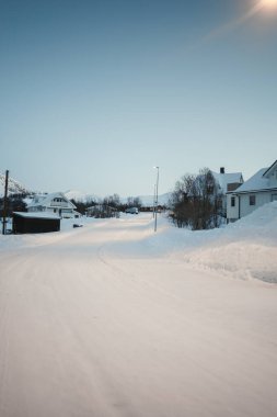 Tromso Norveç yakınlarında, güneş doğarken Ersfjordbotn 'un karlı arktik köyünden geçen yol.