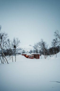 Finlandiya 'nın Kilpisjarvi kentinde göl kenarındaki karlı dağın önündeki kırmızı kulübe..