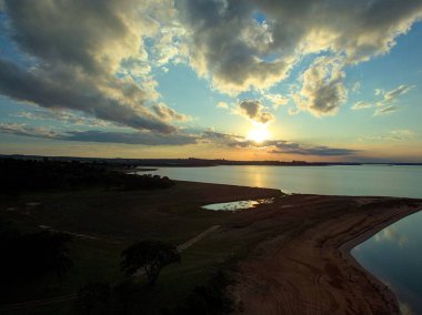 Gün batımında mavi gökyüzü barajın kenarında ağaçların gölgesinde.