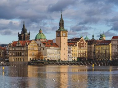 Bulutlu bir günde Charles Köprüsü 'nden kısa bir mesafede, Vltava Nehri' nin setindeki kuleleri olan tarihi evlerden oluşan bir sıra. İnsanlar, arabalar, kuğular ve martılar. Saat kulesi. Prag, Çek Cumhuriyeti, Avrupa