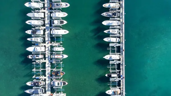 Botlar, yatlar ve sürat tekneleriyle dolu bir marinanın hava görüntüsü, berrak mavi sularla dolu canlı ve hareketli bir rıhtım manzarası, eğlence ve eğlence için mükemmel.