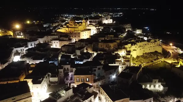 İtalya, Ostuni 'nin nefes kesici gece manzarası. Fotoğraf, bu güzel İtalyan kasabasının aydınlık sokaklarını ve binalarını yakalıyor ve geceleri tarihi mimarisini ve cazibesini sergiliyor.