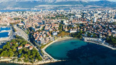 Hırvatistan 'ın Split kentindeki Bacvice plajının hava manzaralı bir manzarası, manzaralı kıyı şeridi ve turkuaz suları yakalıyor. Bu fotoğraf, yaz tatili atmosferiyle ünlü canlı plajı gösteriyor.