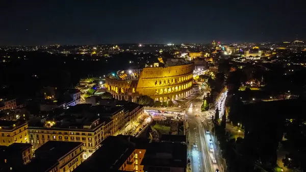 Gece Roma 'daki Kolezyum' un çarpıcı hava manzarası, akşam gökyüzüne karşı güzelce aydınlatılmış. Fotoğraf, Roma 'nın göbeğindeki bu ikonik antik anıtın ihtişamını yansıtıyor.
