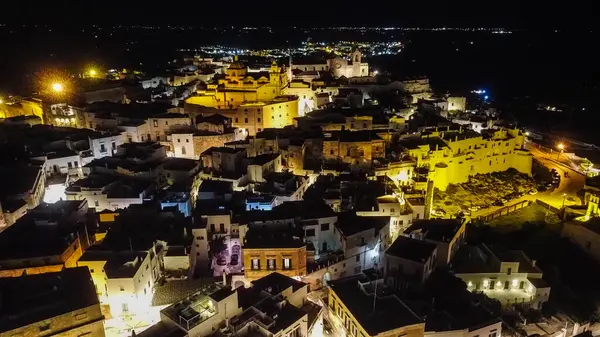 Gece vakti İtalya 'nın Ostuni kentinin çarpıcı hava manzarası akşam gökyüzünün altında ışıldayan büyüleyici beyaz şehri gözler önüne seriyor. Fotoğraf bu ikonik kasabanın güzelliğini ve tarihsel mimarisini vurguluyor.