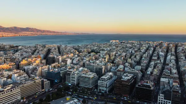 Yunanistan 'ın Atina kıyı bölgesi, gün batımında, Akdeniz sularını aydınlatan yumuşak altın ışıkla ve ikonik gökdelenlerle. Atinalı sahillerde sakin bir akşam