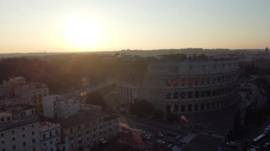 Roma, İtalya 'daki Kolezyum' un güneşli bir gününde, parlak güneş ışığıyla yıkanan simgesel antik amfi tiyatronun görkemli mimarisini ve etrafını çevreleyen tarihi şehir manzarasını yakalıyor.