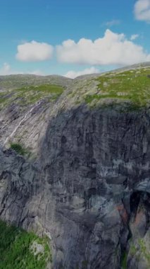 Göz kamaştırıcı bir manzara, açık mavi gökyüzünün altında canlı yeşilliklerle çevrili yüksek uçurumları gösteriyor.