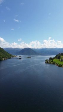 Berrak mavi gökyüzünün altında yemyeşil dağlarla çevrili sakin bir gölün nefes kesici manzarası.