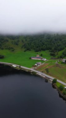 Nefes kesici bir hava manzarası, yemyeşil tepeler ve yukarıdaki yumuşak, sisli bulutlarla çevrili sakin bir gölü yakalar.