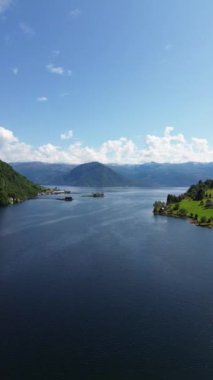Berrak mavi gökyüzünün altında yemyeşil dağlarla çevrili sakin bir gölün nefes kesici manzarası.